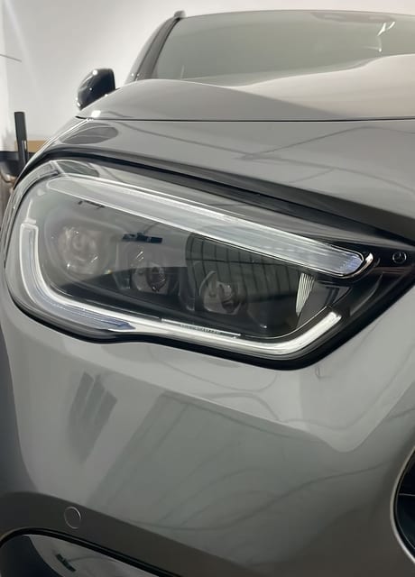 Primer plano frontal del faro de LED moderno y detallado de un automóvil de color gris, situado dentro de un taller o garaje.