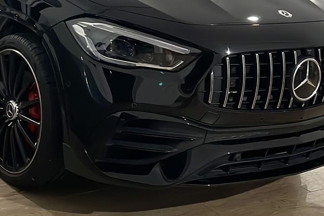 Vista frontal detallada de un deportivo Mercedes-Benz de color negro, con un enfoque nítido en la parrilla Panamericana con el emblema, el faro y la llanta con pinza de freno roja.