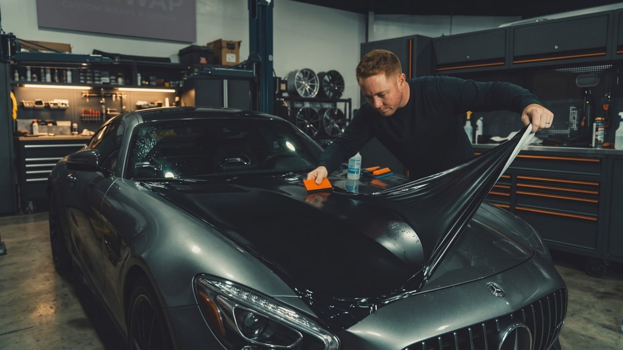 Jean, especialista de JM Detailing, instalando film de protección de pintura (PPF) en el capó de un Mercedes-AMG en su taller.
